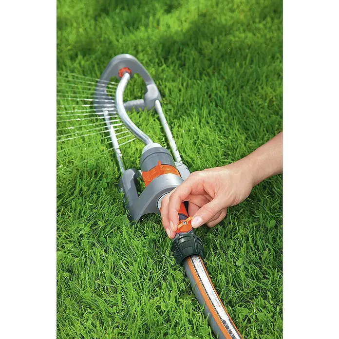 Gardena Regulierstop - Größe: ¾″ - Gartenbewässerung: Eine Hand bedient einen Gardena Regner auf einem grünen Rasen.