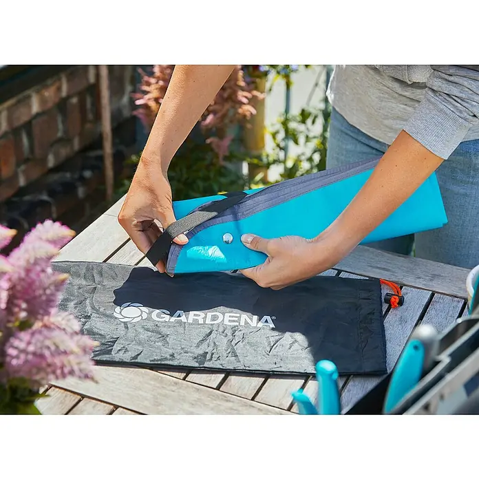 Gardena Pflanzmatte City Gardening - 100 x 120 cm - Eine Person rollt eine hellblaue Gardena Gartenmatte zusammen, während sie über einer schwarzen Aufbewahrungstasche liegt.