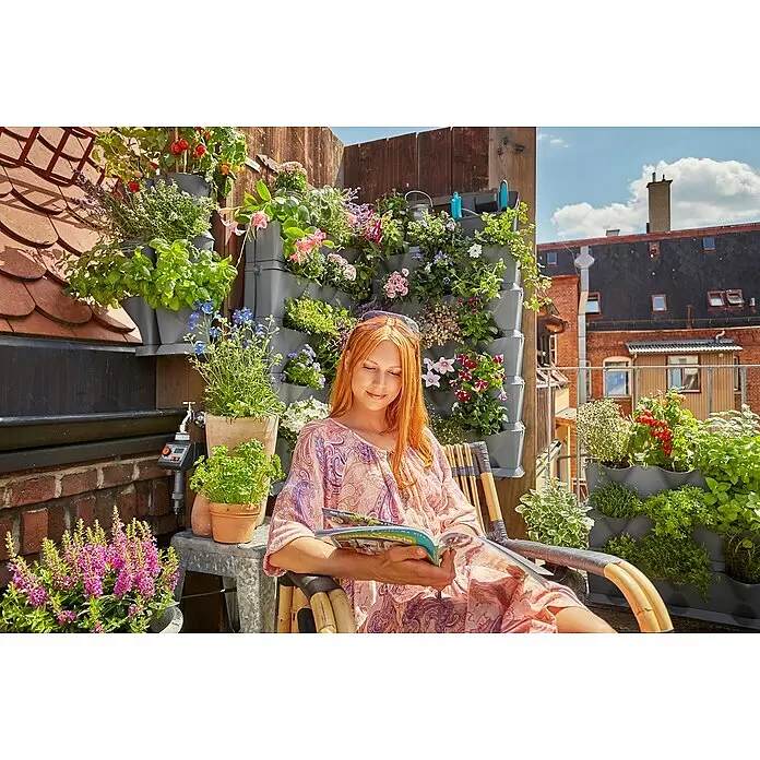 Gardena Verbinder-Set NatureUp! - Passend für: Gardena NatureUp! Pflanzgefäße, 8 Stk. - Graue modulare Vertikalpflanzgefäße auf einem Balkon, gefüllt mit verschiedenen Pflanzen und Blumen. Eine Frau liest daneben und genießt die grüne Oase.