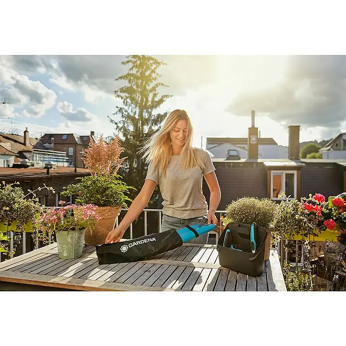 Gardena Pflanzmatte City Gardening - 80 x 80 cm - Frau packt GARDENA Gartengeräte auf einem Holztisch aus, umgeben von Pflanzen und einem sonnigen Hintergrund.
