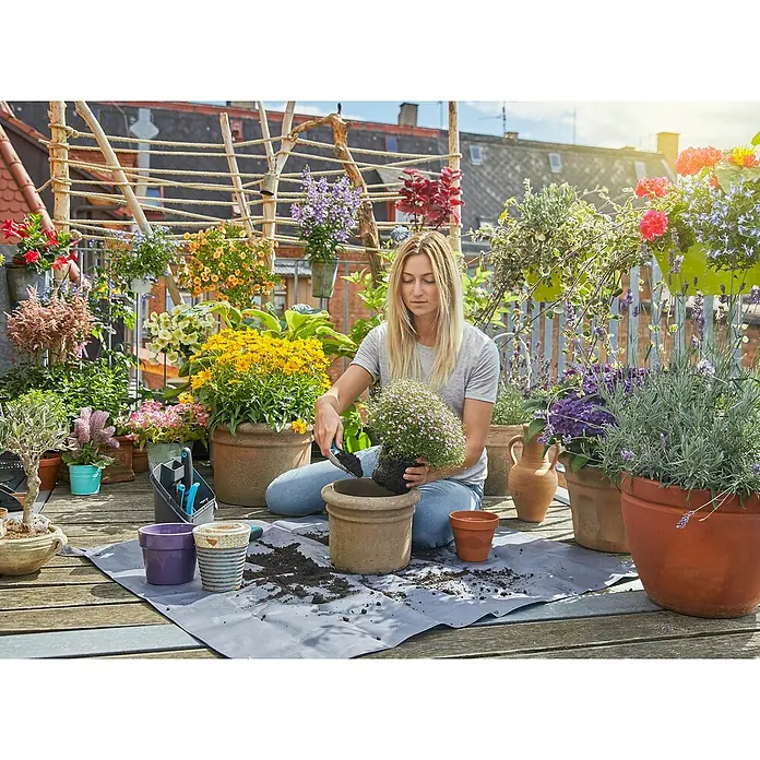 Gardena Pflanzmatte City Gardening - 100 x 120 cm - Eine Frau pflanzt Blumen auf einer begrünten Terrasse. Die vielen Blumenkästen und Töpfe sind dekorativ und ansprechend.