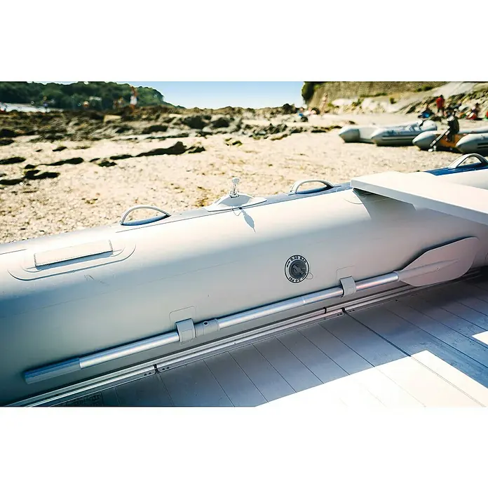 Honda Marine Schlauchboot T35-AE3 - L x B: 353 x 171 cm, Geeignet für: Max. 5 Personen, Nutzlast: 700 kg - Detailaufnahme eines grauen Schlauchbootes am Strand mit Ruder und Haltegriffen, ideal für Wassersport und Freizeitaktivitäten am Meer.
