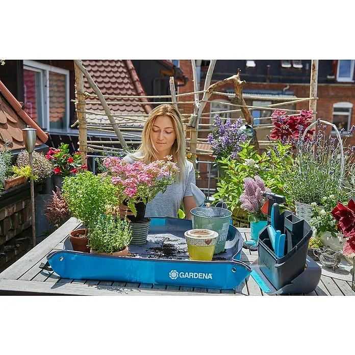 Gardena Pflanzmatte City Gardening - 80 x 80 cm - Eine Frau, die auf einem Balkon mit verschiedenen Pflanzen und einem blauen Gardena Pflanzhelfer gärtnert.