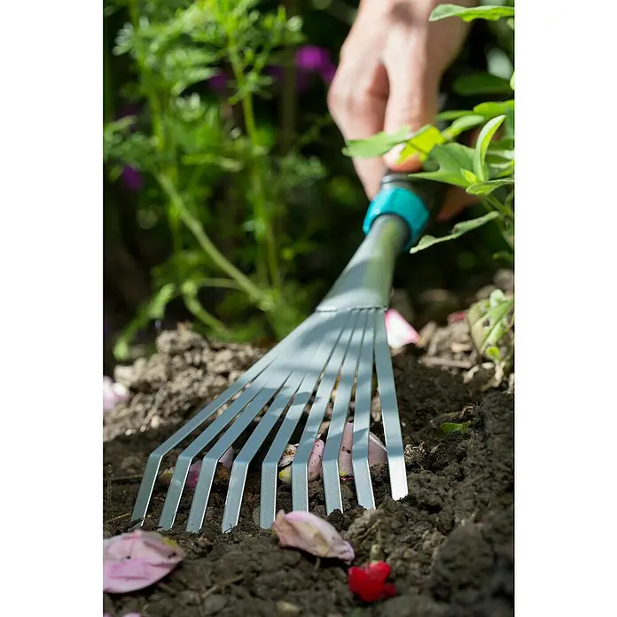 Gardena Comfort Kleingeräte-Set - 3 -tlg. - Nahaufnahme einer Hand, die einen Fächerbesen in einem Garten verwendet, um gefallene Blütenblätter zu entfernen.