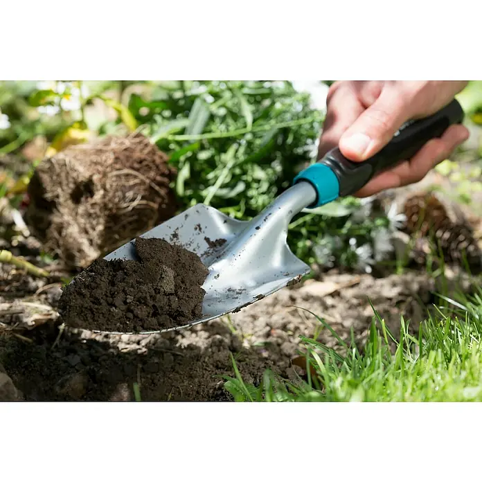 Gardena Comfort Kleingeräte-Set - 3 -tlg. - Nahaufnahme einer Gartenschaufel mit Erde, gehalten von einer Hand, ideal für Gartenarbeiten und zur Bodenbearbeitung im Garten.