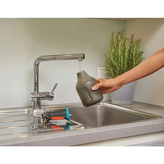Gardena Drucksprüher Set - Bestehend aus: Drucksprüher Comfort 5 l & Pumpsprüher 0,75 l - Eine Gardena Blumenspritze wird unter einem Wasserhahn in einer Küchenspüle mit Wasser befüllt, daneben eine Sprühpistole.