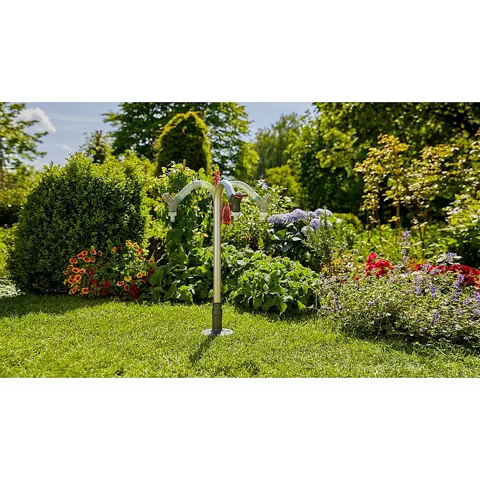 Gardena Sprinklersystem Wasserhahn - Metall - Gartenszene mit einem GARDENA Wasserverteiler mit zwei Hähnen, eingebettet in üppiges Grün und farbenfrohe Blumen, ideal für die Gartenbewässerung.