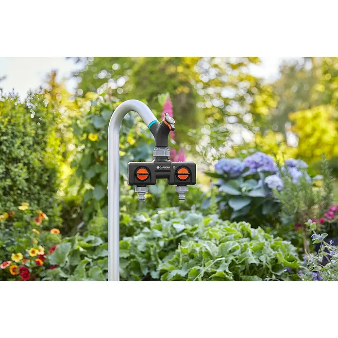 Gardena Sprinklersystem Wasserhahn - Metall - Nahaufnahme eines Gardena Wasserverteilers mit zwei Ausgängen, ideal für die Gartenbewässerung, umgeben von üppigem Grün und bunten Blumen.