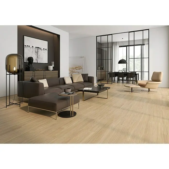Pavimento porcelánico Bosco - 22,5 x 119,5 cm, Primavera, Mate, Rectificado - Un salón moderno con un sofá de cuero marrón, una mesa de centro y un elegante sillón sobre un suelo de madera clara. La lámpara elegante completa el diseño.