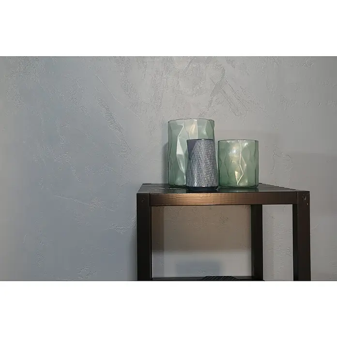 SCHÖNER WOHNEN-Farbe Betondesign-Optik Versiegelung - Grau, 1 l, Passend für: SCHÖNER WOHNEN-Farbe Betondesign-Optik Flächenspachtel - Dekoratives Stillleben mit grünen Glasvasen und einem grauen Ornamentbehälter auf einem stilvollen, dunklen Tisch vor einer grauen Wand.