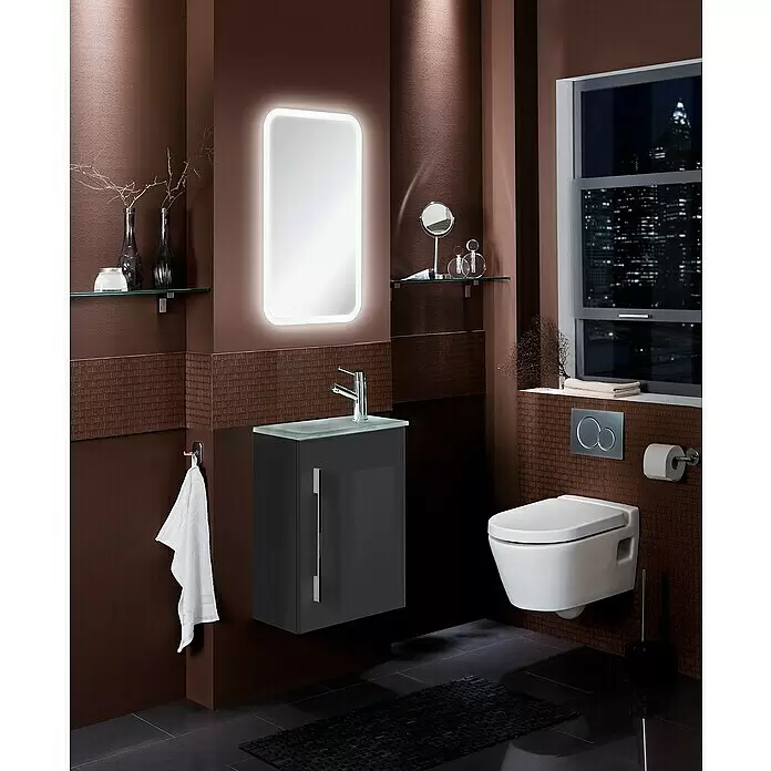 Camargue Stella Mini Badmöbel-Set SM45G - Gesamtbreite Badmöbel: 45 cm, Grafit, Hochglänzend, 3 -tlg. - Modernes Bad mit dunkelbraunen Wänden, beleuchtetem Spiegel, Wand-WC und schwebendem Waschtisch, mit Stadtblick bei Nacht.