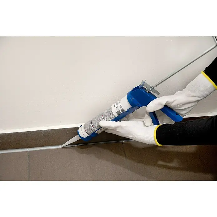Alpha Tools Kartuschenpresse - Ohne Zahnstange, Geeignet für: Silikon - Eine Kartuschenpistole, die weiße Dichtungsmasse zwischen einer Wand und Fliesen aufträgt, wobei der Fokus auf der Pistole und dem Auftrag liegt.