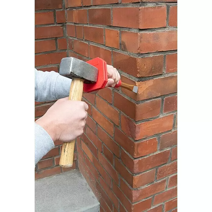Wisent Handschutzgriff - Material: Gummi - Eine Person benutzt einen Mauerbeitel mit rotem Handschutz und Hammer an einer Ziegelwand.