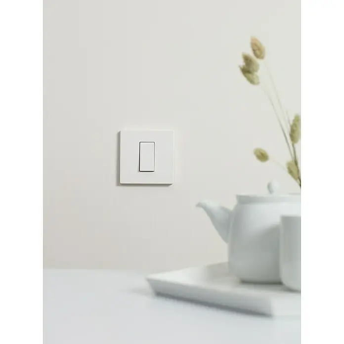 Simon 270 Conmutador Kit - Blanco, 10 A, Colocar - Primer plano de un interruptor de luz blanco en una pared, junto a una tetera y una taza, transmitiendo una estética minimalista.