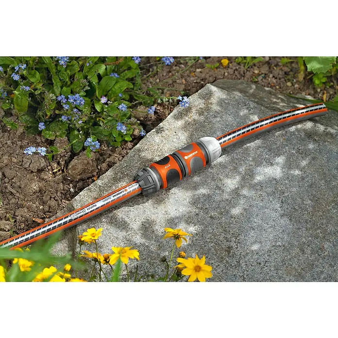 Gardena Schlauchkupplung - Grau - Nahaufnahme eines Gardena-Schlauchs mit orangefarbenem Verbinder auf einem Stein, umgeben von Blumen.