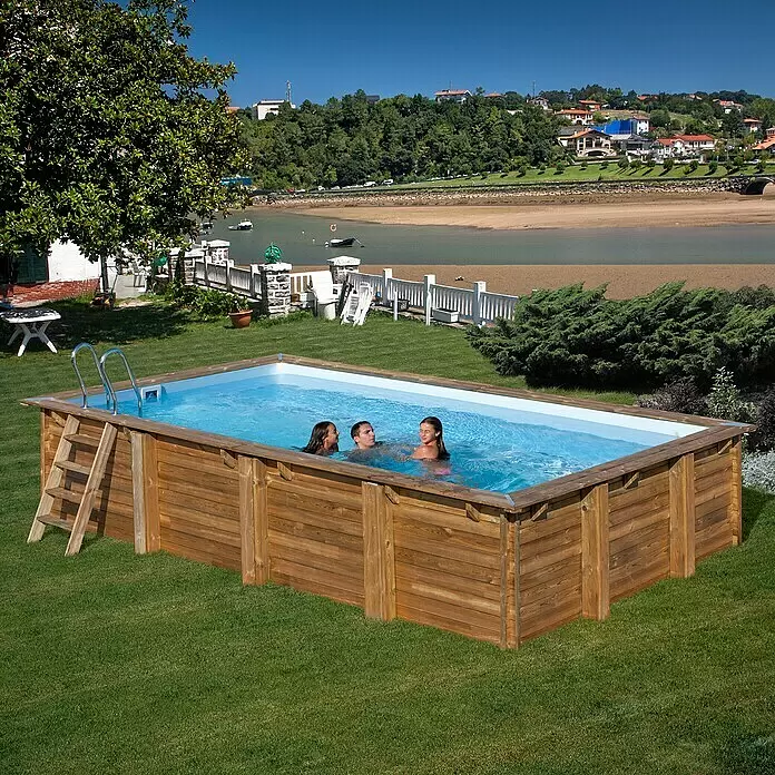 Gre Holz-Pool Evora - L x B x H: 600 x 400 x 133 cm, Hellbraun, 23.500 l - Ein oberirdischer Holzschwimmbecken mit drei Personen, die im sonnigen Garten am Fluss das Wasser genießen.