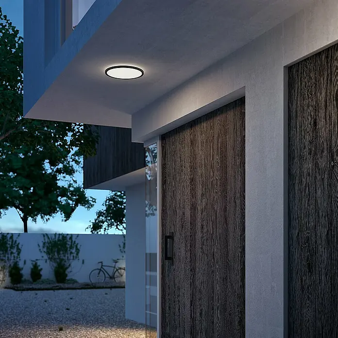 Philips Plafón LED redondo SuperSlim - 15 W, Ø x Al: 25 x 2,3 cm, Negro, Blanco, Blanco neutro - Una moderna lámpara de techo de perfil bajo con borde negro ilumina la entrada de una casa en la oscuridad.
