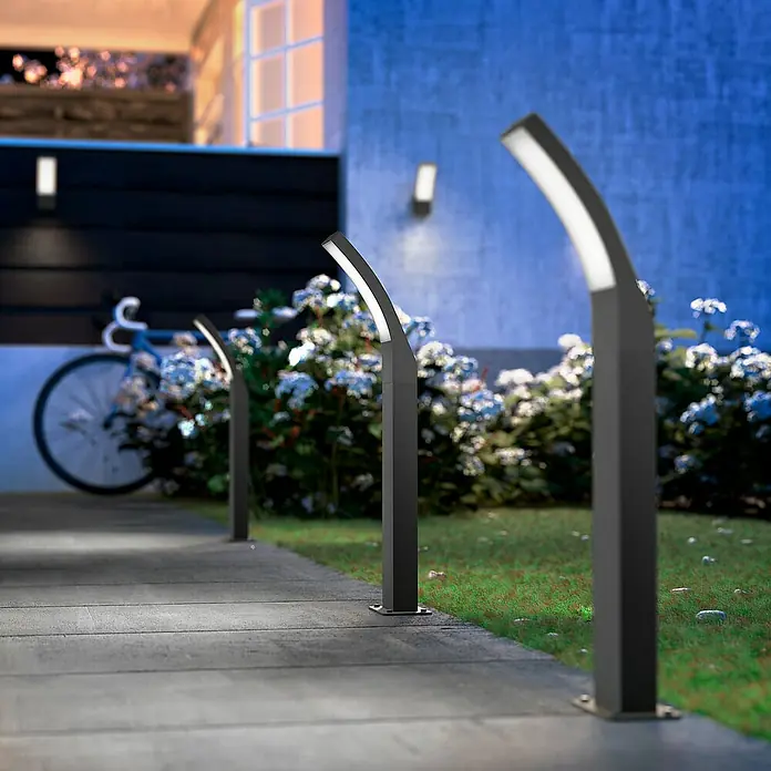 Philips Splay Sobremuro exterior - Color del marco: Antracita, Blanco frío, Con bombillas, Altura: 60 cm - Luces de jardín iluminadas bordean un camino, creando un ambiente exterior moderno y elegante.