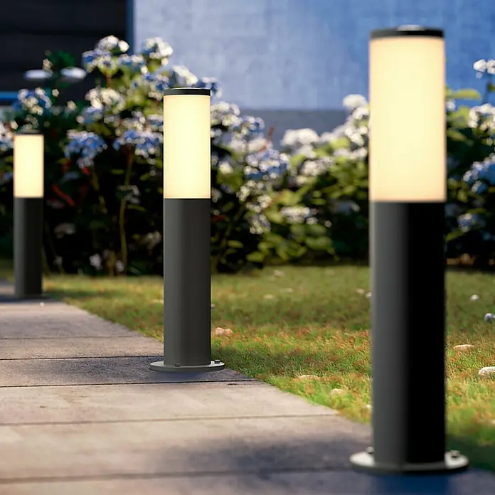 Philips LED-Sockelleuchte Utrecht - 20 W, Anthrazit, 12 x 12 x 45 cm - Nahaufnahme von drei modernen Außenleuchten, die einen Gehweg säumen und ein warmes Licht abgeben. Die Beleuchtung betont den Garten.