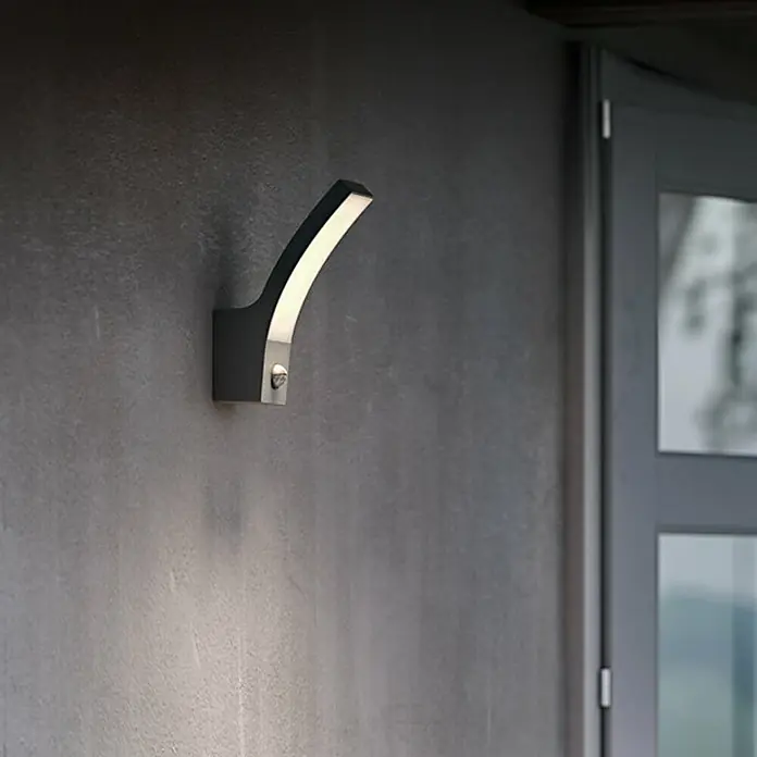 Philips Splay Aplique exterior con sensor - 12 W, L x An x Al: 16,1 x 8 x 24 cm, Antracita, Blanco frío - Luz de pared LED moderna con diseño curvo, proyectando una luz cálida en una pared oscura. Montada junto a una puerta, iluminación exterior ambiental.