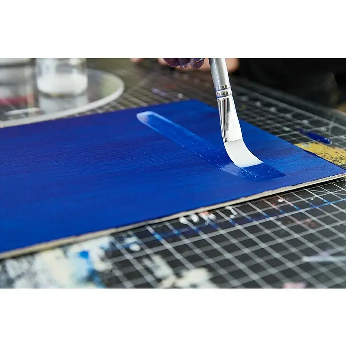 Liquitex Basics Flachpinsel - Größe Pinsel: 2, Nylonfaser, Holz - Nahaufnahme von weißer Farbe, die mit einem Pinsel auf ein blau gestrichenes Brett aufgetragen wird, um künstlerische Akzente zu setzen.