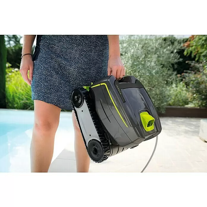 Zodiac Robot de piscina Tornax GT2120 - Funcionamiento en red, Piscinas 8 x 4 m, 11 m³/h - Persona sosteniendo un limpiafondos robótico Tornax gris y verde lima con orugas junto a una piscina.