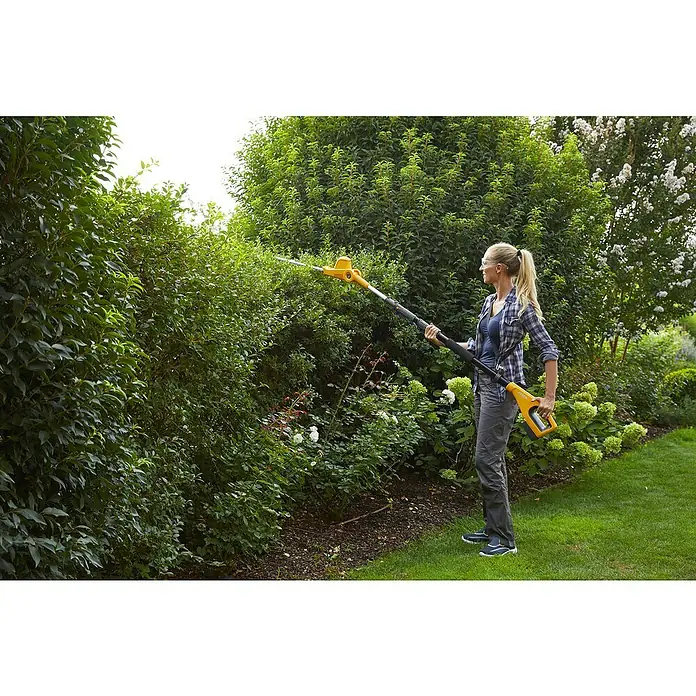 Stiga Akku-Multitool MT 100e Set - 20 V, 1 Akku, Schnittlänge: 41 cm - Eine Frau benutzt eine STIGA Akku-Heckenschere zum Trimmen einer hohen Hecke im Garten.