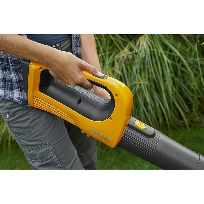 Stiga Soplador de hojas de batería BL 100e Kit - 20 V, 1 batería, 4 Ah, Velocidad de soplado: 115 km/h, Potencia de soplado: 9 m³/min - Primer plano de un soplador de hojas amarillo STIGA sostenido por una persona al aire libre, centrándose en el diseño ergonómico.
