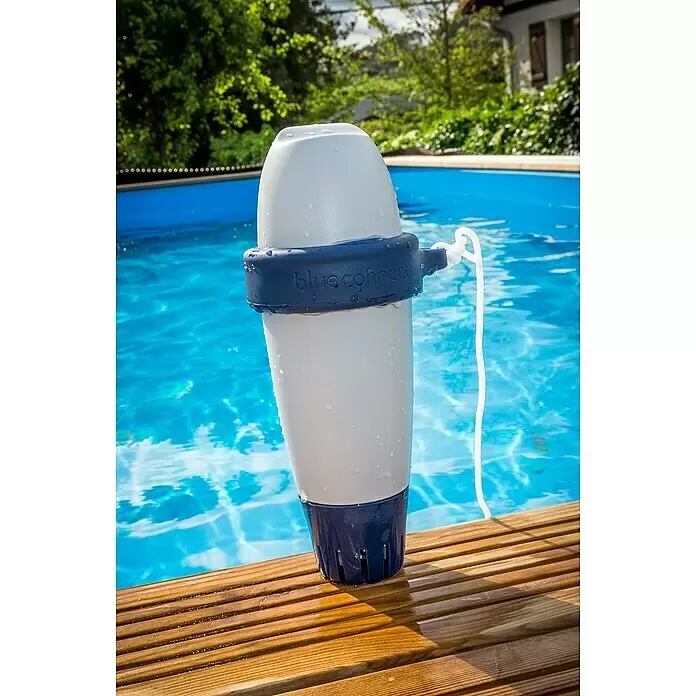 Fluidra Blue Connect Wasser-Analysegerät - Steuerung per Smartphone-App - Weißer und blauer „blue connect“ Smart Pool Analysator, nass, auf Holzdeck neben Swimmingpool.