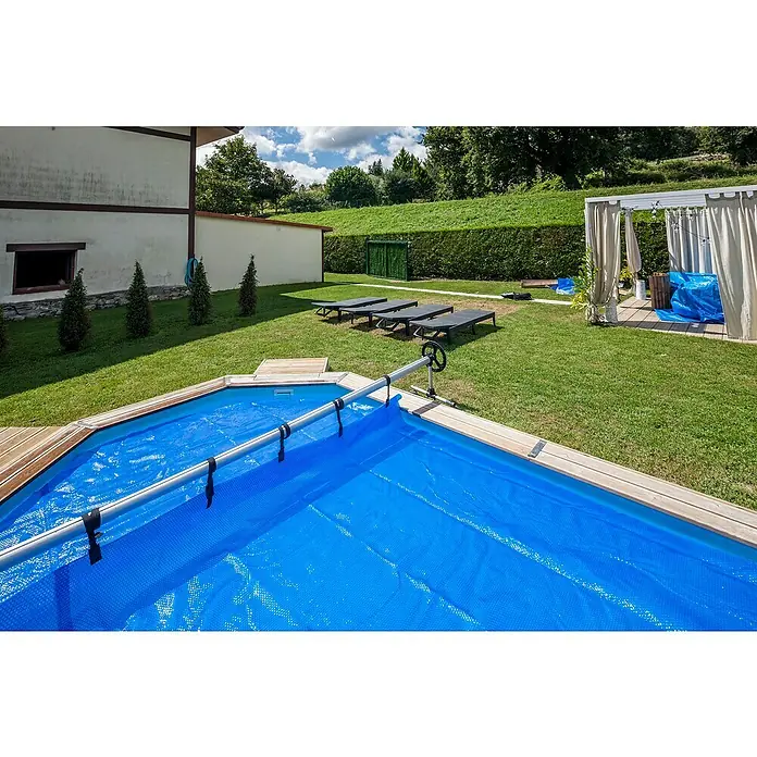 Gre Planenaufroller - Passend für: Pools bis 500 cm Breite - Abgedecktes Schwimmbad im Garten mit Solarplane, Holzdeck und Aufrollvorrichtung neben Liegestühlen unter einem Pavillon.