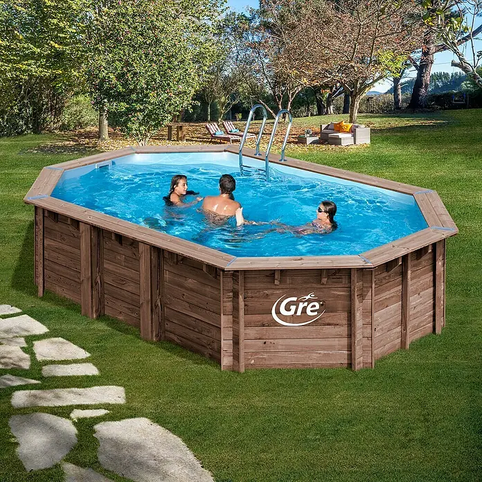 Gre Holz-Pool Macadamia - L x B x H: 632 x 335 x 130 cm, Naturbraun, 17.900 l - Dieses Bild zeigt einen Gre-Holzpool mit drei Personen im Wasser, umgeben von einer grünen Rasenfläche und Bäumen.