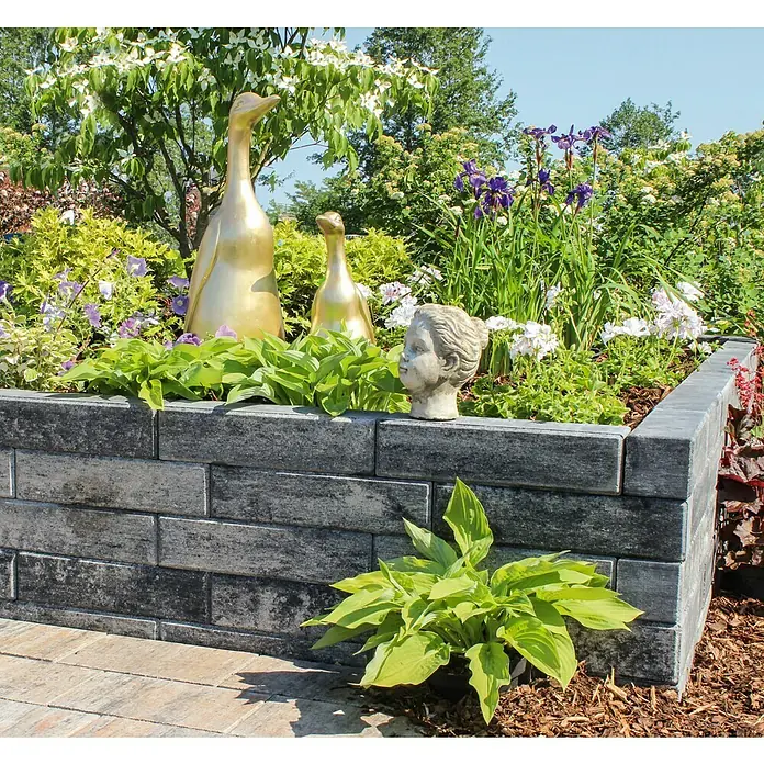 Diephaus Palisade / Mauerstein Laredo - 40 x 10 x 10 cm, Weiß/Schwarz, Beton - Dekorativer erhöhter Garten mit Ziegelsteinen, goldenen Entenstatuen und einer Kopfskulptur in einem malerischen Garten.