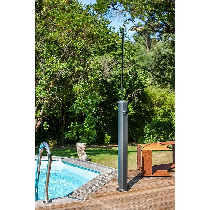 Gre Ducha solar Esencial Deluxe - Altura: 223 cm, Aluminio, Antracita - Una ducha de piscina de metal moderna se alza sobre una terraza de madera junto a una piscina, rodeada de exuberante vegetación.