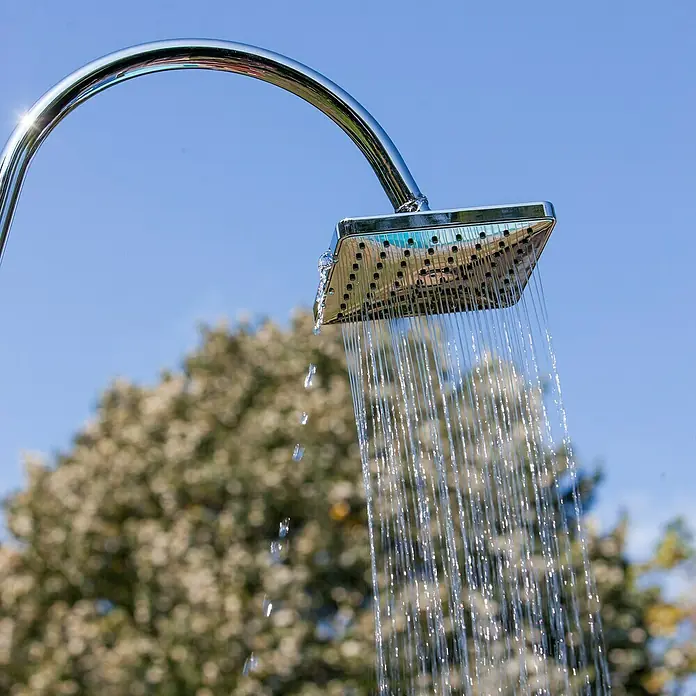 Gre Ducha solar Esencial Deluxe - Altura: 223 cm, Aluminio, Antracita - Ducha al aire libre: Un cabezal de ducha cromado, cuadrado y brillante con agua que fluye, con cielo azul y árboles.