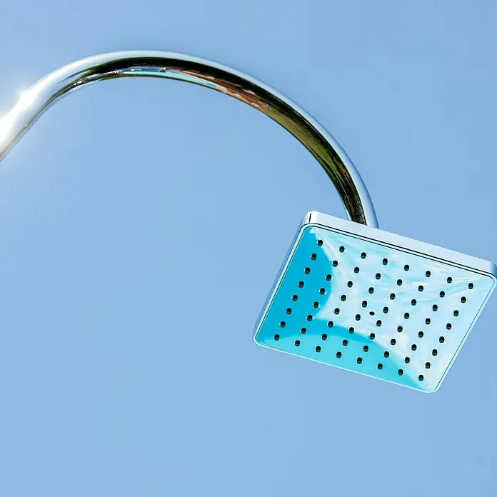 Gre Ducha solar Esencial Deluxe - Altura: 223 cm, Aluminio, Antracita - Primer plano de un cabezal de ducha cuadrado cromado sobre un cielo azul claro, mostrando su diseño moderno.