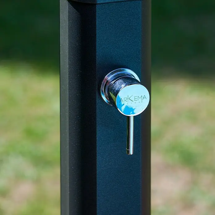 Gre Ducha solar Esencial Deluxe - Altura: 223 cm, Aluminio, Antracita - Primer plano de una ducha exterior negra de ARKEMA con un grifo cromado sobre un fondo verde.