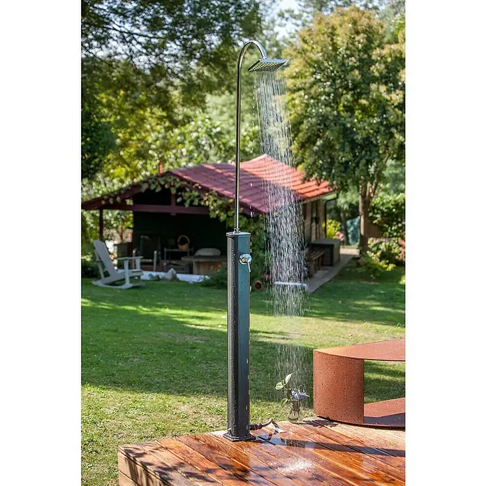 Gre Ducha solar Esencial Deluxe - Altura: 223 cm, Aluminio, Antracita - Ducha exterior con agua rociando sobre una plataforma de madera, ideal para el jardín. Al fondo, una caseta con techo rojo.