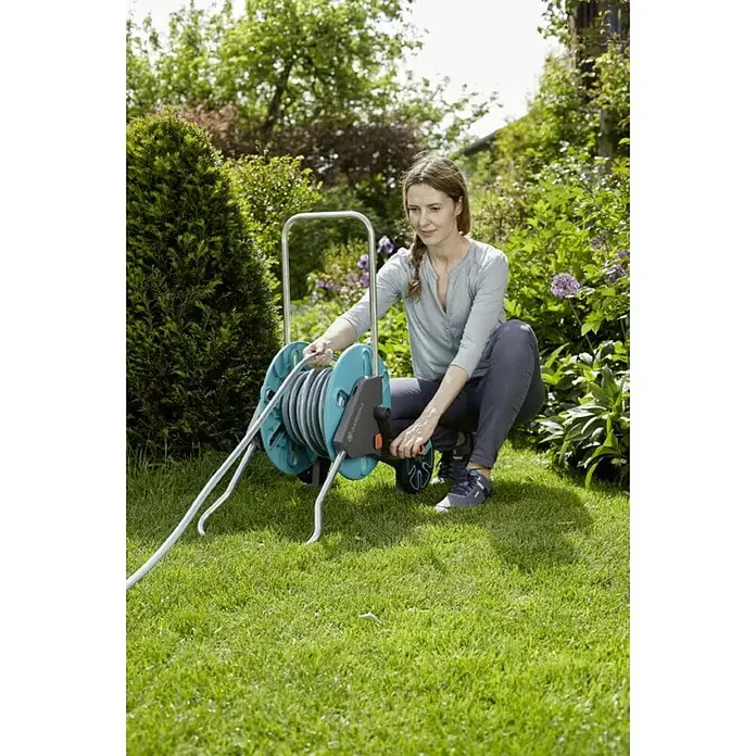 Gardena Schlauchwagen CleverRoll M - Kunststoff/Metall, Schlauchkapazität: 60 m, 13 mm (½″) - Eine Frau bedient eine Gardena Schlauchtrommel im Garten, um ihren Rasen zu bewässern.