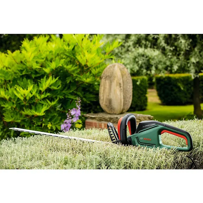 Bosch Elektro-Heckenschere UniversalHedgeCut 60 - 480 W, Schnittlänge: 60 cm - Eine grüne Bosch Heckenschere liegt auf einer Hecke im Garten, bereit für den Einsatz, um Sträucher und Pflanzen zu pflegen und in Form zu bringen.
