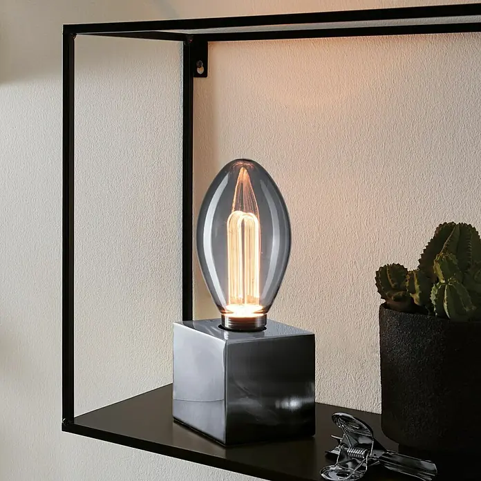 Paulmann Inner Glow LED-Lampe Vintage Glühlampenform E27 - E27, Nicht Dimmbar, Gelb, 80 lm, 3,5 W, Kerze, Farbe: Smoky - Nahaufnahme einer modernen Tischleuchte mit grauem Glasschirm und quadratischem Sockel auf einem schwarzen Regal.