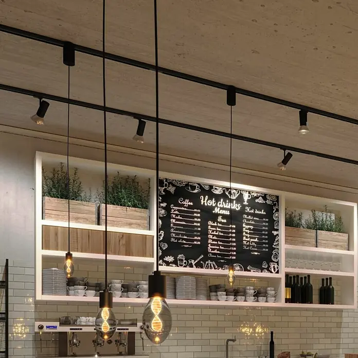 Paulmann Inner Glow LED-Lampe Vintage Glühlampenform E27 - E27, Nicht Dimmbar, Gelb, 90 lm, 3,5 W, Kerze, Farbe: Smoky - Das Bild zeigt eine moderne Café-Beleuchtung mit schwarzen Schienenstrahlern und dekorativen Edison-Glühbirnen.