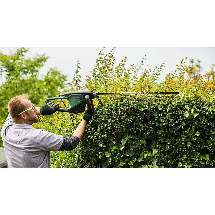 Bosch Elektro-Heckenschere AdvancedHedgeCut 70 - 500 W, Schnittlänge: 70 cm - Ein Mann schneidet eine Hecke mit einer Bosch Heckenschere. Das grüne Elektrowerkzeug schneidet präzise die Äste.