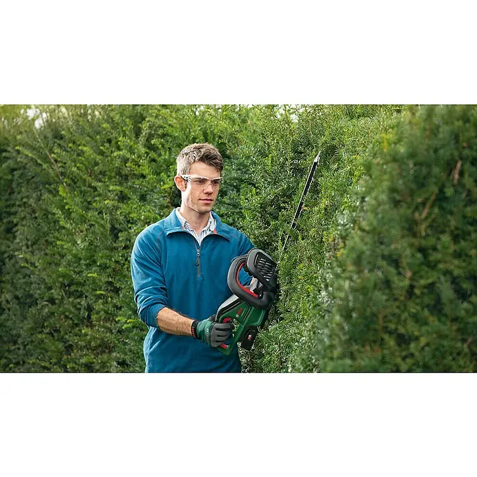 Bosch Power for All 18V Akku-Heckenschere UniversalHedgeCut 18V-55 - 18 V, Li-Ionen, Ohne Akku, Schnittlänge: 50 cm - Ein Mann mit Schutzbrille stutzt eine Hecke mit einer Bosch-Heckenschere, wobei der Fokus auf der Heckenschere liegt.