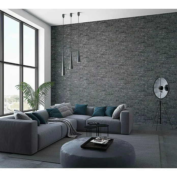 Marburg Sand & Stones Vliestapete Steinmauer I - Grau/Dunkelgrau, Steinoptik, 10,05 x 0,53 m - Wohnzimmer mit grauer Couch, Ziegelwand und Stehlampe.