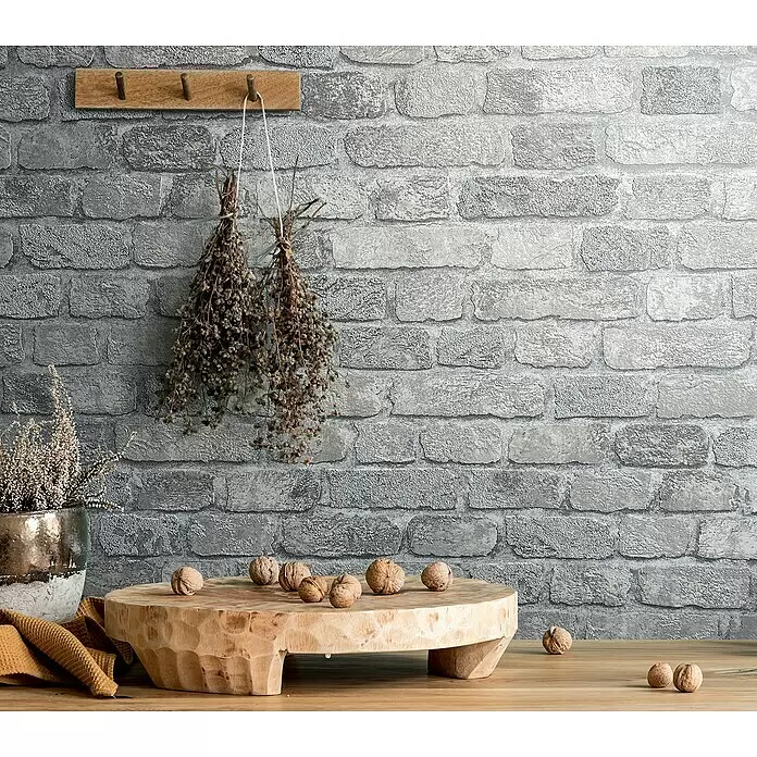 Marburg Sand & Stones Vliestapete Steinmauer II - Grauweiß, Steinoptik, 10,05 x 0,53 m - Strukturierte graue Tapete mit Ziegelmuster, die eine rustikale und industrielle Kulisse in einem Raum bildet.