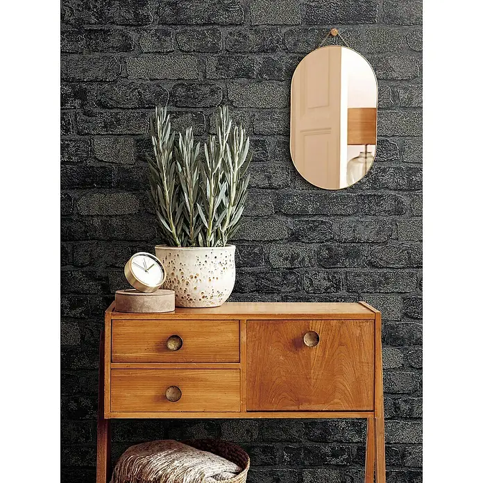 Marburg Sand & Stones Vliestapete Steinmauer I - Grau/Dunkelgrau, Steinoptik, 10,05 x 0,53 m - Stilvolles Sideboard aus Holz mit Schubladen und einem Schrank, dekoriert mit einer Pflanze, einer Uhr und einem Spiegel an einer Backsteinwand.