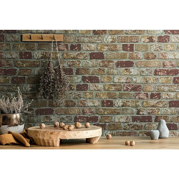 Marburg Sand & Stones Vliestapete Steinmauer II - Beige, Steinoptik, 10,05 x 0,53 m - Nahaufnahme eines rustikalen Interieurs mit Backsteinmauer, Holzbrett mit Nüssen, Topfpflanze und dekorativen Accessoires.