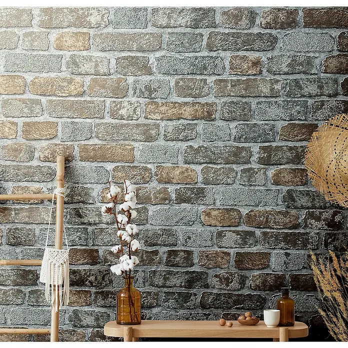 Marburg Sand & Stones Vliestapete Steinmauer II - Graubeige, Steinoptik, 10,05 x 0,53 m - Nahaufnahme einer Wand mit dekorativer Backsteintapete, ergänzt durch eine Holzleiter und eine Vase mit Baumwollzweigen.