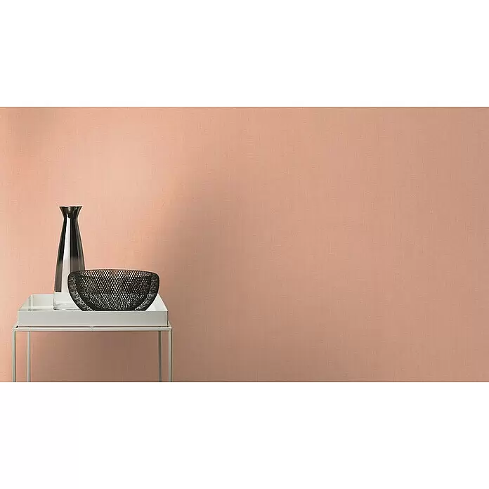 Rasch Florentine III Vliestapete - Rosa, Uni, 10,05 x 0,53 m - Pfirsichfarbene Wand mit feiner Stoffstruktur, akzentuiert durch Vase und Gitterkorb auf weißem Tisch.