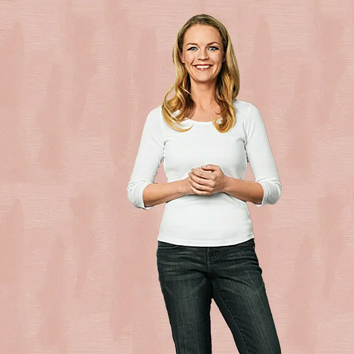 SCHÖNER WOHNEN-Farbe Trendstruktur Farbeffektputz Metall-Optik Effektfarbe - Roségold, Glänzend, 1 l - Freundliche Frau mit blondem Haar trägt ein weißes Langarmshirt und Jeans vor einem rosafarbenen Hintergrund.